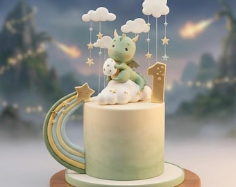 May include: A whimsical birthday cake featuring a green dragon perched on a cloud, holding an egg. The cake is decorated with a rainbow, stars, and the number "1". The cake has a gradient green and white color scheme and sits on a wooden base.