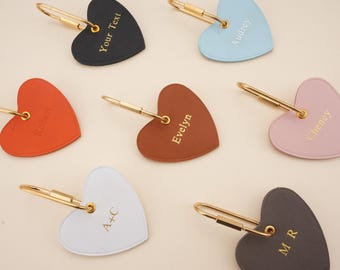 May include: A collection of seven heart-shaped tags in black, light blue, orange, brown, pink, white, and dark gray. Each tag features a gold-toned metal clasp and is engraved with custom text including names like Robert, Evelyn, Audrey, Cheney, A+C, M R, and Your Text.