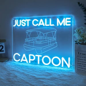 May include: A blue neon sign with white lettering that reads "JUST CALL ME CAPTOON". The sign features a cartoon image of a pontoon boat.
