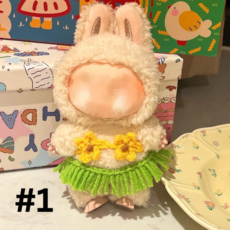 May include: A plush bunny doll wearing a fluffy cream-colored hooded outfit with bunny ears. It has a yellow flower necklace and a green grass skirt. The number "#1" is printed in black at the bottom.