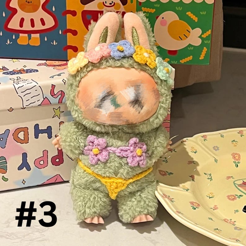 May include: A plush doll in a green fuzzy bunny suit with a flower crown and a yellow and pink crochet bikini. The doll has a painted face and is standing next to a yellow floral plate. The number "#3" is in the bottom left corner.