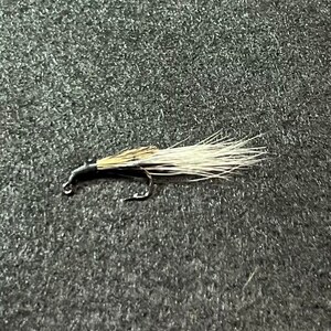 Puede incluir: Un señuelo de pesca con mosca negro y blanco con una cola de plumas blancas.