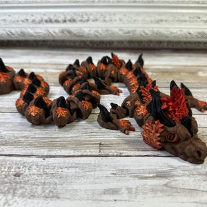 May include: A small, hand-crafted dragon figurine made of polymer clay. The dragon is brown and orange with black accents and has a curled tail.
