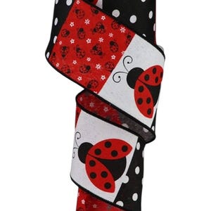 May include: A decorative ribbon spool featuring a repeating pattern of ladybugs, polka dots, and floral accents. The ribbon has a white background with red and black designs. The ladybug ribbon is perfect for crafts and gift wrapping.