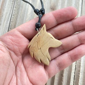 Op de afbeelding: Halsketting met een houten hanger in de vorm van een wolfskop. De lichtbruine hanger hangt aan een zwart koord. De wolfskop is ingewikkeld gesneden en het koord is verstelbaar.