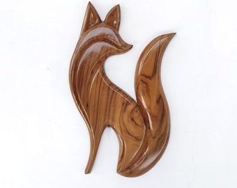 May include: A wooden fox sculpture with a smooth, polished finish. The fox is depicted in a standing pose with its tail curved upwards. The sculpture is a warm brown color and appears to be made from a single piece of wood.
