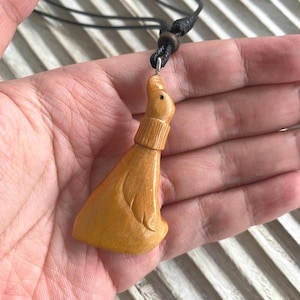 May include: A carved wooden pendant necklace featuring a seal design. The pendant is a light brown color and is suspended from a black cord. The seal has detailed carving and a textured appearance.