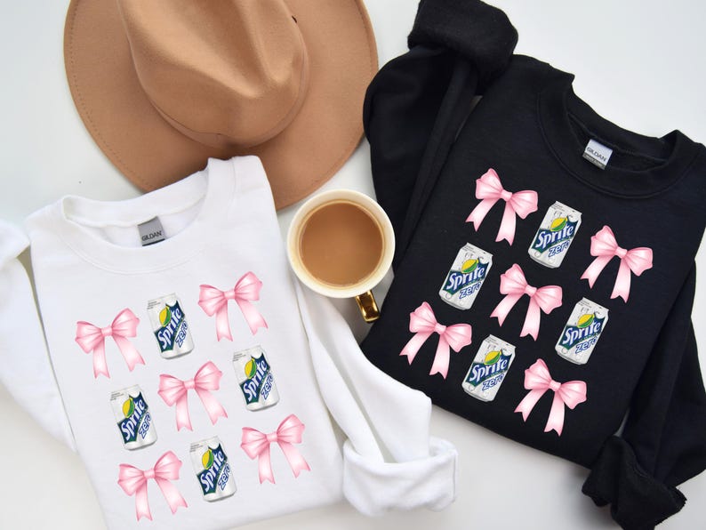 Op de afbeelding: Twee witte en zwarte sweatshirts met een grafische print van roze strikken en blikjes Sprite. De tekst op de blikjes luidt "Sprite Lemon Lime".