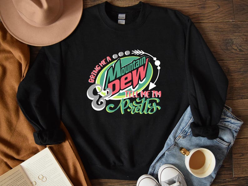 Puede incluir: Sudadera negra con un logotipo de Mountain Dew verde, rojo y blanco y el texto "Bring me a Mountain Dew & tell me I'm pretty".
