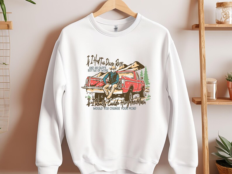 May include: White sweatshirt with a vintage-style graphic of a person sitting in the back of a red pickup truck. The text reads "If I had two dozen roses and an older bottle of wine, If I really coulda hung the moon, would you change your mind."