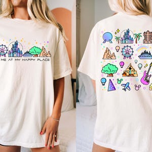 Op de afbeelding: Wit T-shirt met een kleurrijke afbeelding van Disney World bezienswaardigheden en de tekst "Meet me at my happy place".