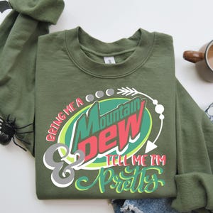 Puede incluir: Sudadera verde de manga larga con un gr&aacute;fico de una lata de Mountain Dew y el texto "Bring me a Mountain Dew & tell me I'm pretty".