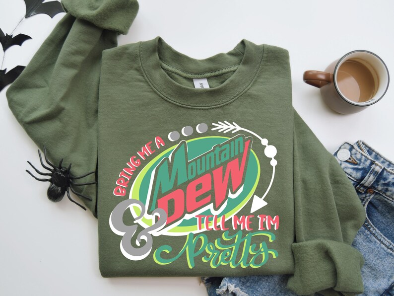 Puede incluir: Sudadera verde de manga larga con un gr&aacute;fico de una lata de Mountain Dew y el texto "Bring me a Mountain Dew & tell me I'm pretty".