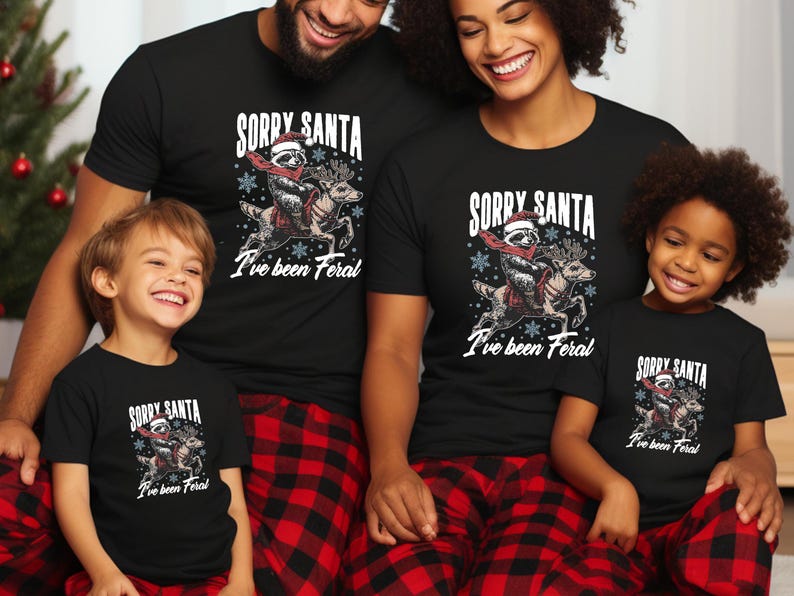 May include: A family of four wearing matching black t-shirts with a graphic of a raccoon riding a reindeer and the text "Sorry Santa I've been Feral". The adults are wearing red and black checked pyjama trousers.