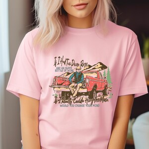 May include: Pink t-shirt with a graphic of a man sitting in the back of a red pickup truck. The text on the shirt reads "If I Had Two Dozen Roses and an Older Bottle of Wine If I Really Coulda Hung The Moon Would You Change Your Mind".