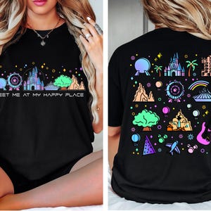Op de afbeelding: Zwart T-shirt met een kleurrijke afbeelding van een Disney-themapark skyline en de tekst "Meet me at my happy place".