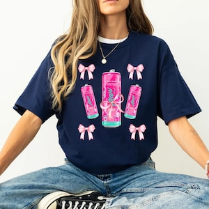 Puede incluir: Una camiseta azul marino con un diseño gráfico rosa y blanco que presenta una lata de agua con gas con el texto "AHA" y lazos rosas.