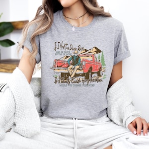 May include: Gray t-shirt with a vintage illustration of a man sitting in the back of a red pickup truck. The text on the shirt reads "If I Had Two Dozen Roses and an Older Bottle of Wine If I Really Could Hang the Moon Would You Change Your Mind".