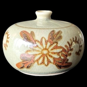 May include: A small, round ceramic vase with a light green glaze and a floral design in shades of brown and orange. The vase has a narrow neck and a crackle finish.