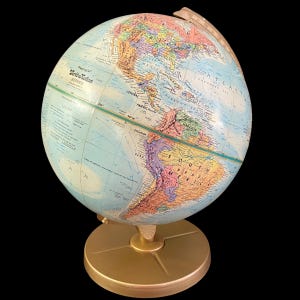 May include: A Replogle World Nation Series globe with a gold-colored base and meridian. The globe features a detailed map with various colors representing different countries and geographical features. The globe is set against a black background.