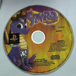 May include: A purple dragon character, Spyro, is featured on the front of a PlayStation game disc. The disc is labeled "Spyro the Dragon" and has a "PlayStation" logo, "NTSC U/C" label, and an "Everyone" ESRB rating.