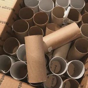 May include: A cardboard box filled with empty cardboard tubes of varying sizes. The tubes are primarily brown and white, with some overlapping. The box is brown and has printed text on the sides.