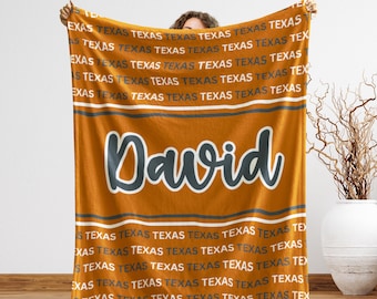 May include: An orange blanket with the name "David" in a large, stylized font. The word "Texas" is repeated in white across the blanket, with gray and white stripes.