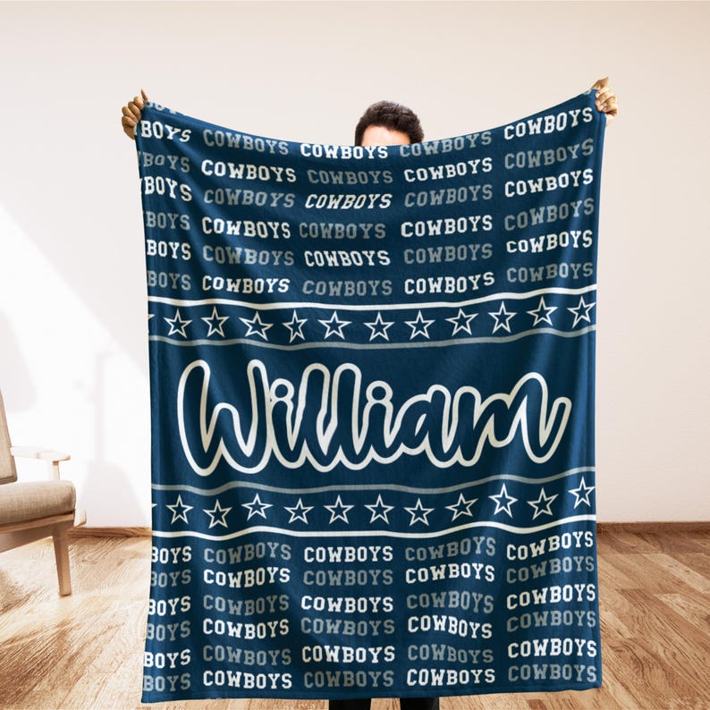 May include: A navy blue blanket with the text "BOYS COWBOYS" repeated across the top and bottom. The name "William" is displayed in a white script font in the center, above a row of white stars.