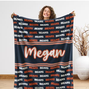 May include: Navy blue blanket with the word "BEARS" in orange and white repeated across the top and bottom. The name "Megan" is displayed in a cursive font in the center of the blanket.
