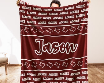 May include: Maroon blanket with the name "Jason" in white script. The blanket features the word "AGGIES" repeated in white, along with white Texas-shaped designs. A cozy and personalized gift.