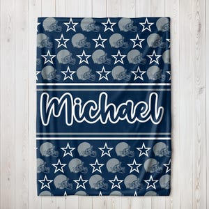 May include: Navy blue blanket with a pattern of gray football helmets and white stars. The name "Michael" is displayed in white script across a navy blue stripe. Two white stripes border the name.