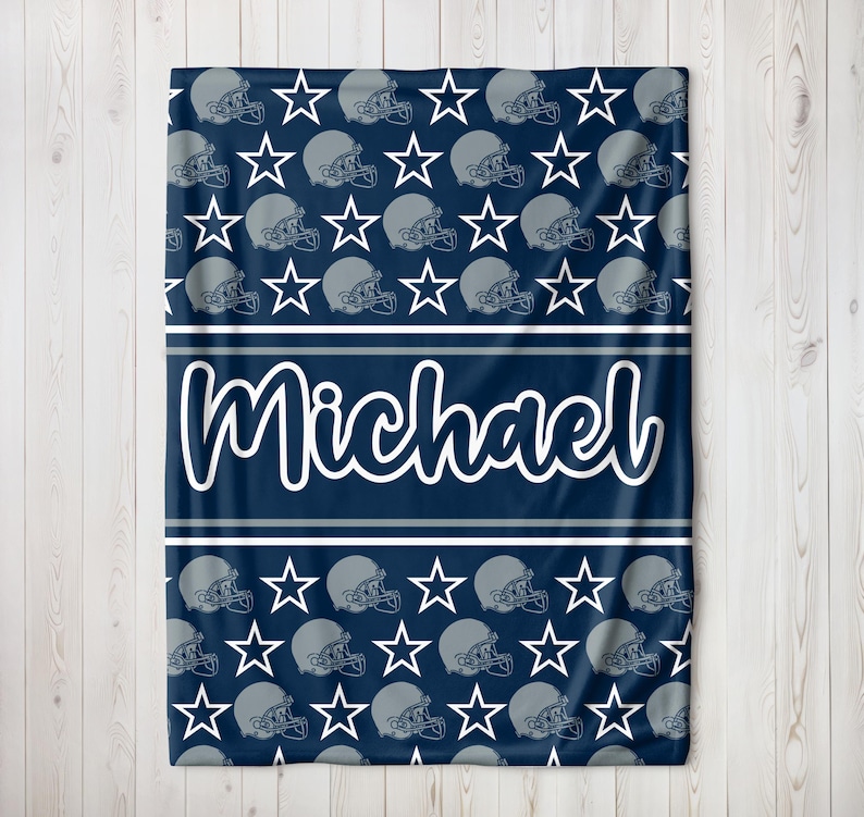 May include: Navy blue blanket with a pattern of gray football helmets and white stars. The name "Michael" is displayed in white script across a navy blue stripe. Two white stripes border the name.