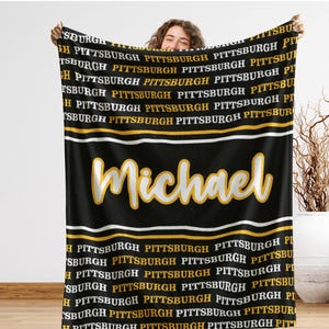 May include: Black blanket with the name "Michael" in yellow script. The word "Pittsburgh" is repeated in white and gold. The blanket has white and gold stripes.