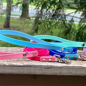 May include: A collection of waterproof dog leashes in various solid colors including light pink, bright pink, sky blue, turquoise, royal blue, and lavender. Each leash features a metal swivel snap hook, rivets, and a D-ring for secure attachment.