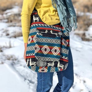 May include: A black and blue shoulder bag with a geometric pattern and llama designs. The bag has a flap with a zipper closure and a small pocket on the front.