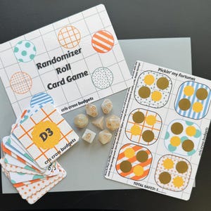 May include: A tabletop game set featuring cards, dice, and a game board. The game includes cards with the text "D3" and "cris cross budgets". The game board has the text "Pickin' my fortunes" and "TOTAL SAVED: $". The dice are translucent with white numbering.