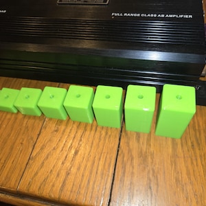 May include: A black audio amplifier with the text "FULL RANGE CLASS AB AMPLIFIER" and a series of bright green rectangular blocks with holes on top. The blocks are arranged in a row, varying in size.