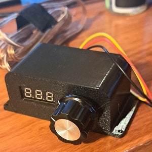 May include: A black electronic device with a digital display showing "8.8.8" and a knob. The device has three wires connected to it, one red, one yellow, and one black.