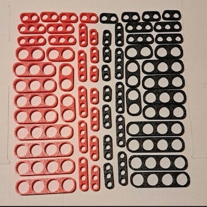 May include: A collection of red and black plastic connectors with multiple holes. The connectors are arranged in rows and columns.