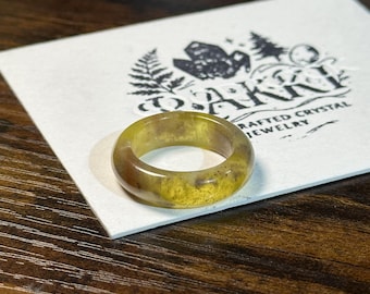 May include: A handcrafted crystal ring with a unique, natural appearance. The ring features a band of translucent yellow and brown tones. The ring is set on a white card with the text "OAKKI Crafted Crystal Jewelry".