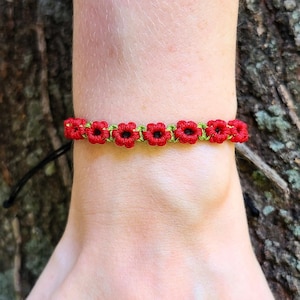May include: A red and green friendship bracelet with a flower pattern. The bracelet is made of string and is tied around a person's wrist.