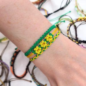 Puede incluir: Tres pulseras de la amistad con hilo verde y amarillo tejido en diseños de flores.