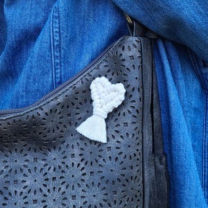 May include: White crocheted heart with a tassel hanging on a black purse with a cut-out design.