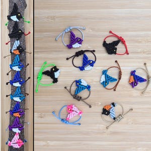 Pode incluir: Uma cole&ccedil;&atilde;o de 12 pulseiras de amizade coloridas com um design de p&aacute;ssaro. As pulseiras s&atilde;o feitas com fio colorido e apresentam p&aacute;ssaros de diferentes cores com olhos pretos.