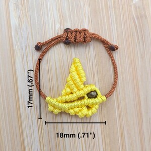 Pode incluir: Um bracelete de amizade amarelo com um design de p&aacute;ssaro e uma conta marrom. O bracelete tem 4,2 cm de altura e 1,8 cm de largura.