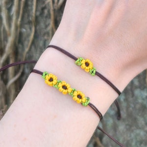 Puede incluir: Dos pulseras de cuerda marrón con abalorios de girasol amarillos y verdes. Las pulseras están atadas a la muñeca de una persona.