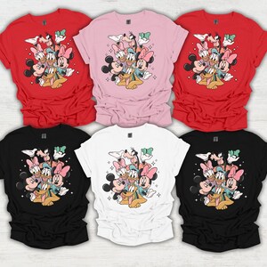 May include: Six t-shirts in various colors: red, pink, black, white. Each shirt features a graphic of Disney characters including Mickey Mouse, Minnie Mouse, Donald Duck, Daisy Duck, Goofy, and Pluto. The design is surrounded by sparkling stars.