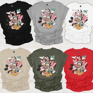 May include: Six t-shirts in various colors: black, gray, white, tan, olive green, and red. Each shirt features a graphic of Mickey Mouse, Minnie Mouse, Donald Duck, Daisy Duck, Goofy, and Pluto. The cartoon characters are clustered together.