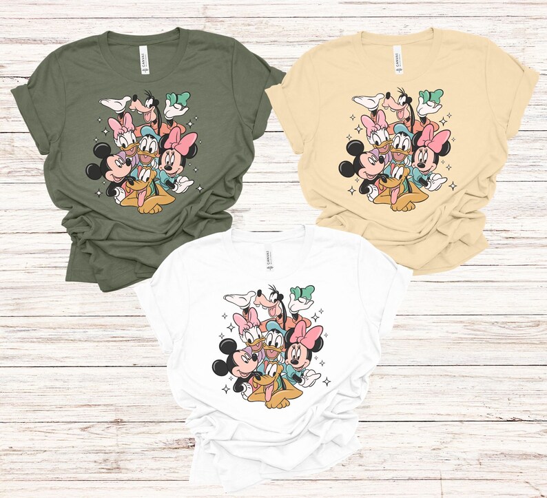 May include: Three t-shirts in olive green, cream, and white, each featuring a colorful graphic of Disney characters including Mickey Mouse, Minnie Mouse, Donald Duck, Daisy Duck, Goofy, and Pluto. The design is surrounded by small starbursts.