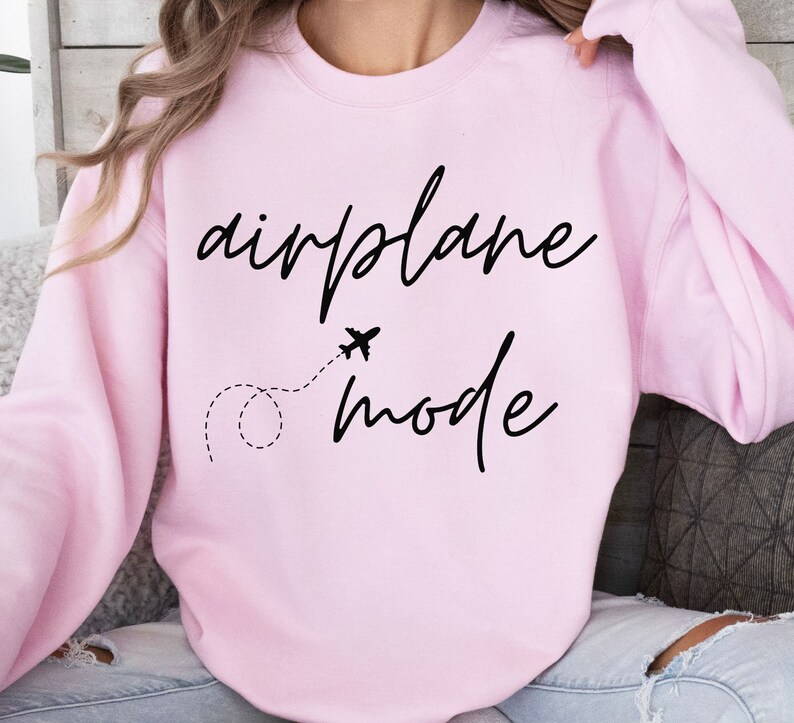Puede incluir: Sudadera rosa claro con las palabras "airplane mode" en fuente negra. Un peque&ntilde;o avi&oacute;n y una l&iacute;nea de puntos est&aacute;n entre las palabras. La sudadera es de cuello redondo.